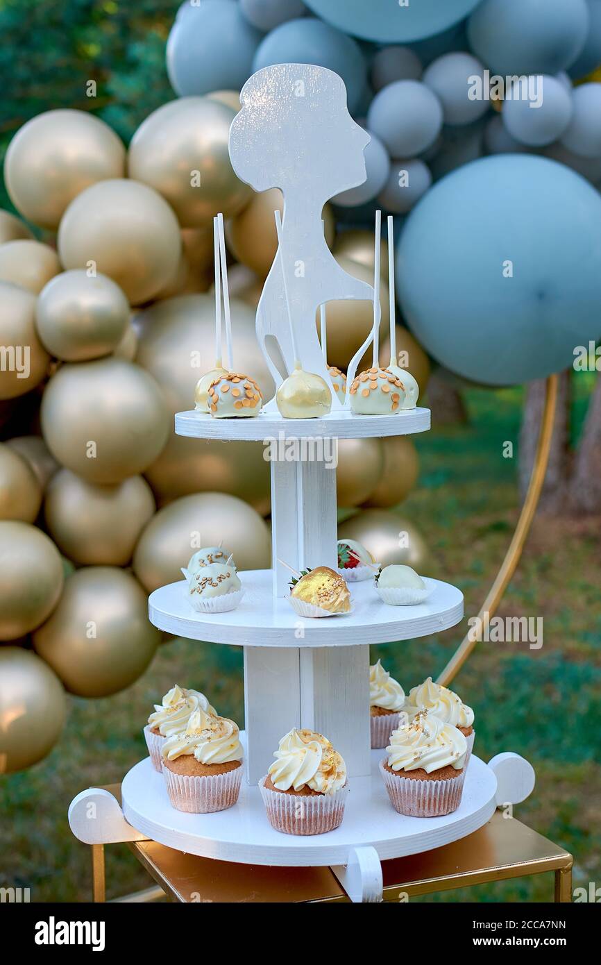 Dessert di nozze su un alto stand. Papi, fragole ricoperte di cioccolato e muffin alla crema. Decorazioni per matrimoni in color oro, decorazioni in palloncino. Foto Stock