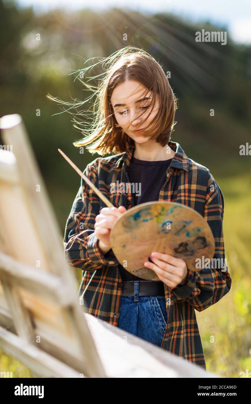 Ritratto di una giovane artista donna che mescola vernice su un palette in una serata estiva di sole su un pliner Foto Stock