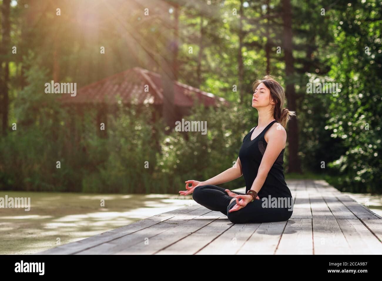 Donna che medita in posizione lotus su passerella in legno all'aperto Foto Stock