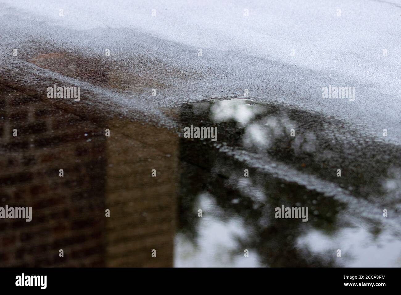 Edificio in mattoni vicino che si riflette in un pozze sul tetto dopo un giorno piovoso Foto Stock