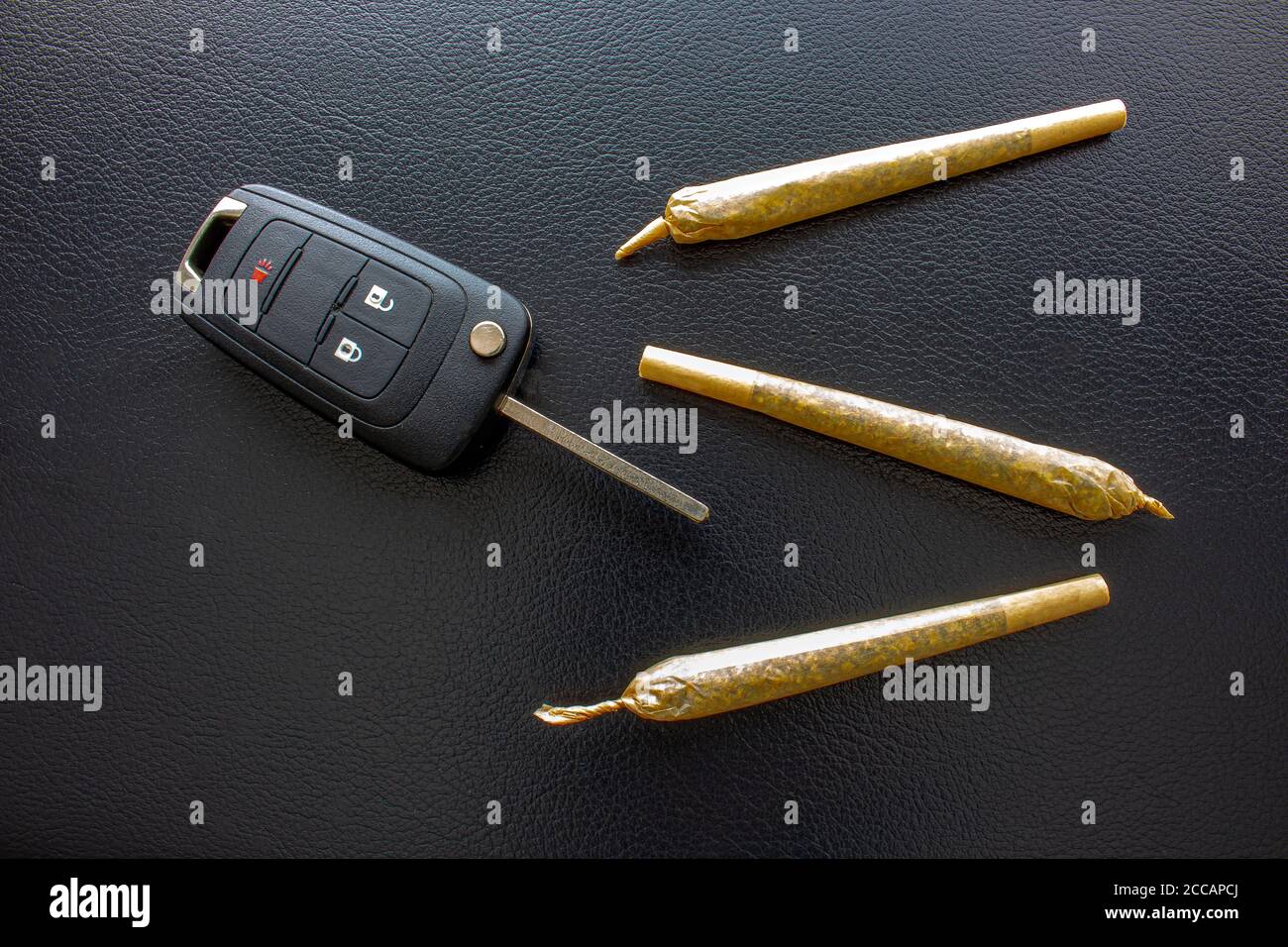 Sigarette con chiave per auto sul lato su una texture nera in pelle. Concetto di guida alta. La guida con problemi di droga è pericolosa e contro il t Foto Stock