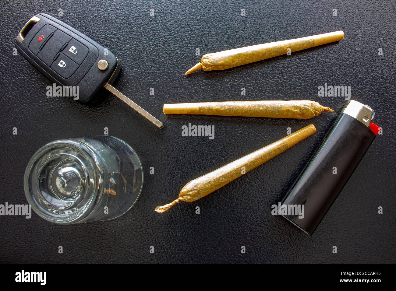 Sigarette con chiave per auto, un bicchiere da sparare e un accendisigari su una texture nera in pelle. Concetto di guida alta. La guida con problemi di droga è pericolosa Foto Stock