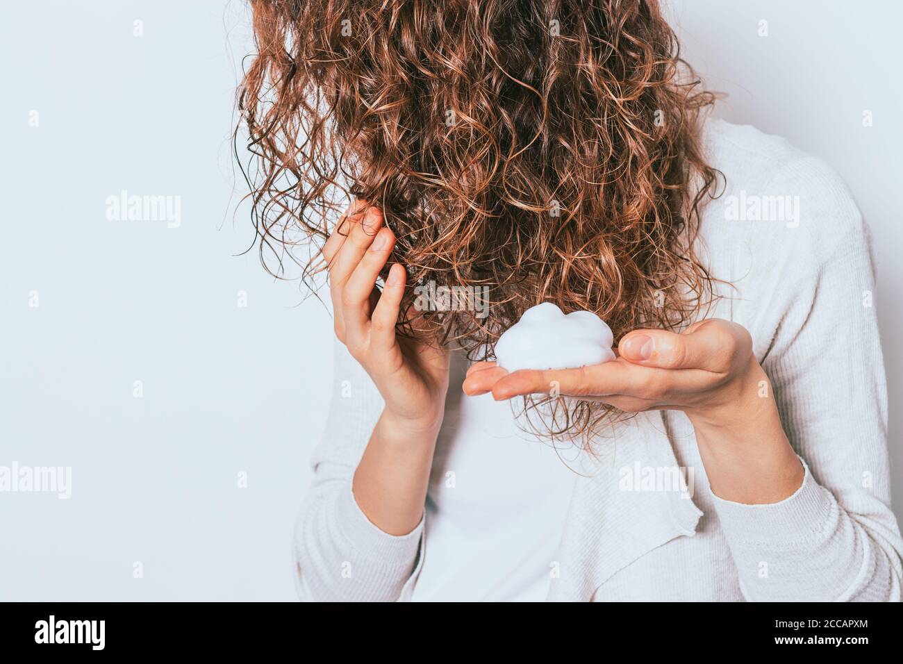 Mousse per lo styling delle mani della donna usata per i suoi capelli ricci bianco sfondo studio Foto Stock
