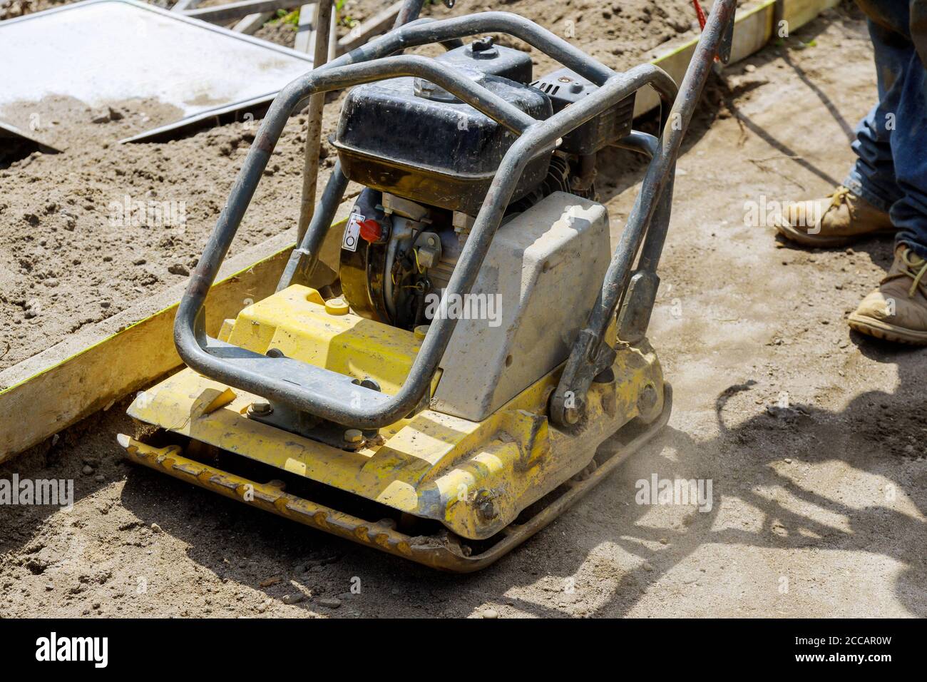 Compattatore a piastre vibranti su una nuova pavimentazione in una macchina industriale da costruzione Foto Stock
