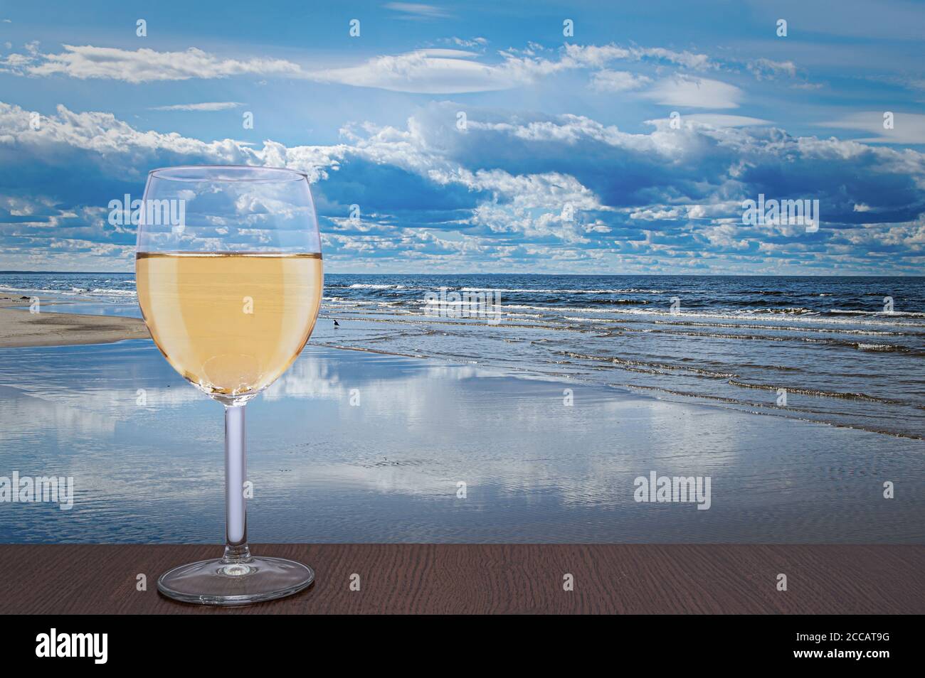 Bicchiere di vino bianco contro il bellissimo paesaggio marino. Mar Baltico durante il giorno di sole con belle nuvole con gabbiani nelle onde a Jurmala, Lettonia Foto Stock