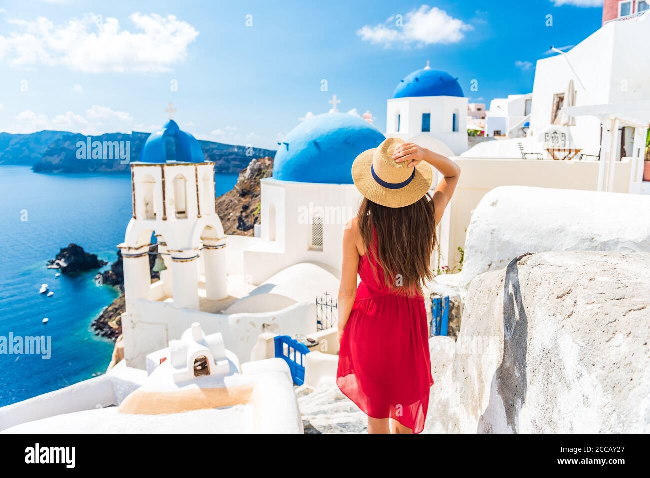 Vacanza di lusso in Europa vacanze Santorini ragazza in cappello e vestito rosso moda a piedi 3 cupole blu famosa attrazione turistica. Estate sole vacanze Foto Stock