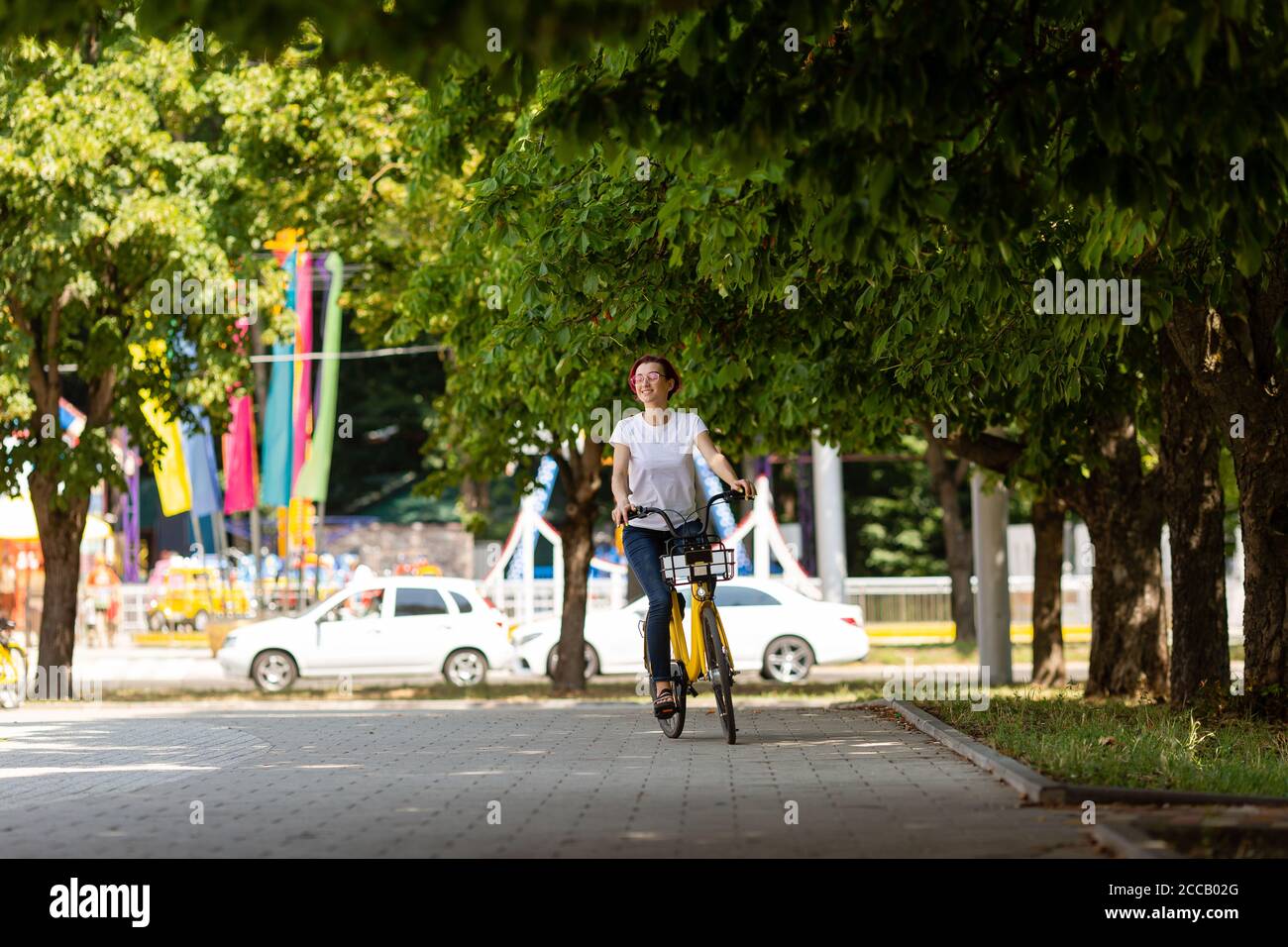 giovane donna con i capelli rosa cammina nel parco con una bicicletta che mangia gelato in estate. Modalità di trasporto ambientale Foto Stock