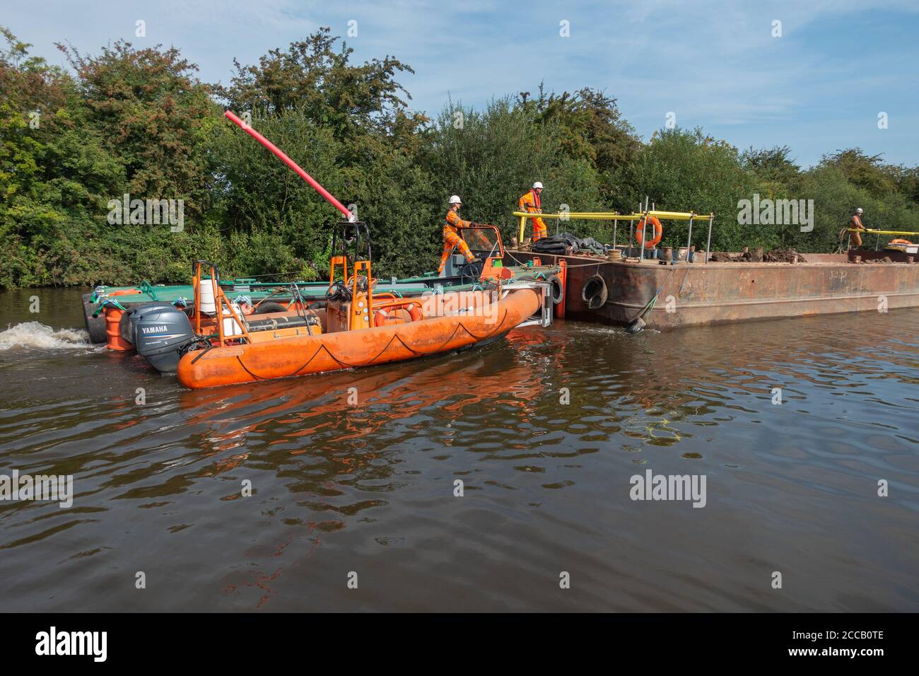 Gli operai di manutenzione del canale e del fiume di CRT spingono una chiatta di rifornimento Con un motoscafo verso un sito di riparazione lungo il fiume a Doncaster Foto Stock