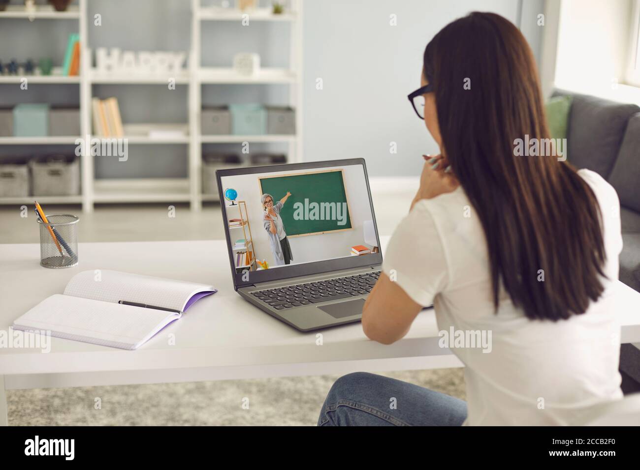 Formazione online. La studentessa ascolta la lezione dell'insegnante ha un computer portatile di videochat seduto al tavolo nella stanza. Foto Stock