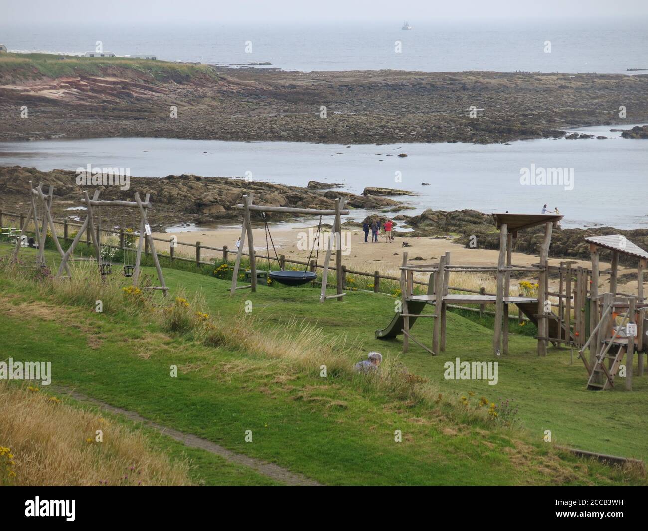 Vista su un parco giochi per bambini vicino alla spiaggia e alle piscine di roccia ai piedi di Kirk Wynd, Crail, Fife Foto Stock