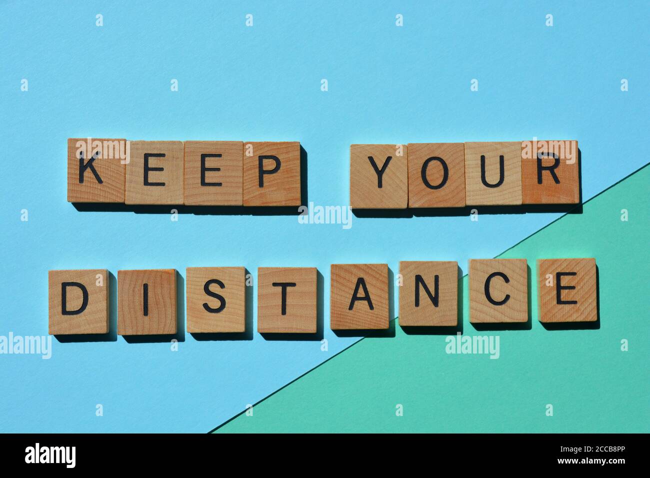 Mantenere la distanza, la frase in caratteri alfabetici in legno 3D isolati su sfondo blu Foto Stock