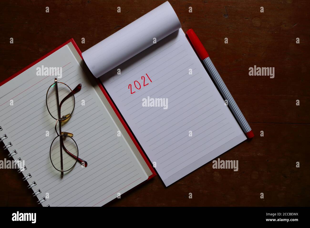 Closeup notebook vuoto con scrittura a mano 2021, occhiali e penna su tavolo in legno, spazio per la copia per la risoluzione di nuovo anno, vista ad alto angolo Foto Stock