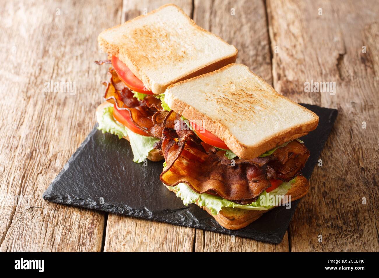 Due panini blt con pancetta, insalata fresca e pomodori sono serviti su una tavola di ardesia sul tavolo. Orizzontale Foto Stock