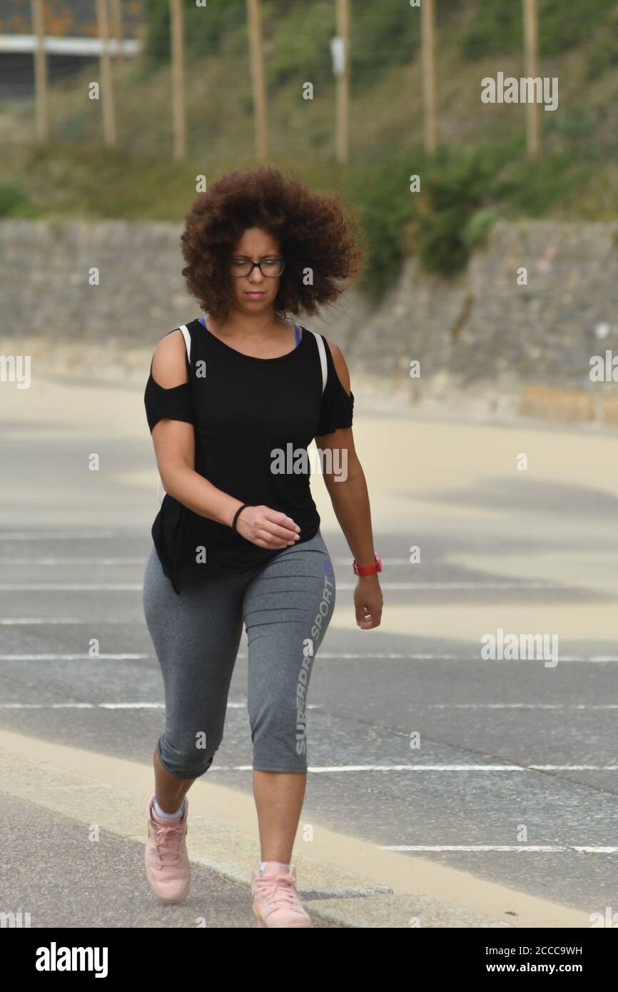 Storm Ellen batte la costa meridionale dell'Inghilterra al culmine della stagione estiva delle vacanze con raffiche di vento fino a 60 mph e un'alta marea. Una donna dai capelli boschi è soffiata dal vento sulla passeggiata, Boscombe, Bournemouth, Dorset, UK, 21 agosto 2020 Foto Stock