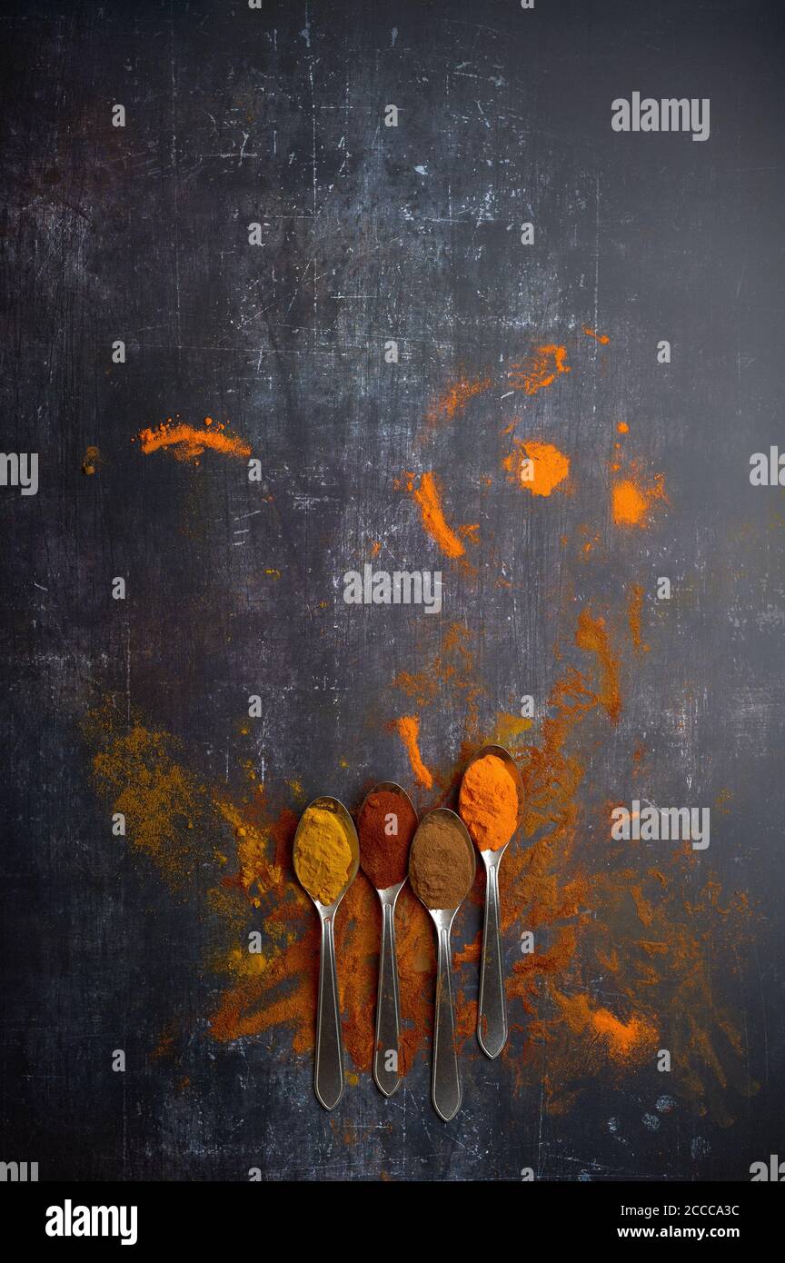 cucchiai con spezie assortite versate su sfondo scuro Foto Stock