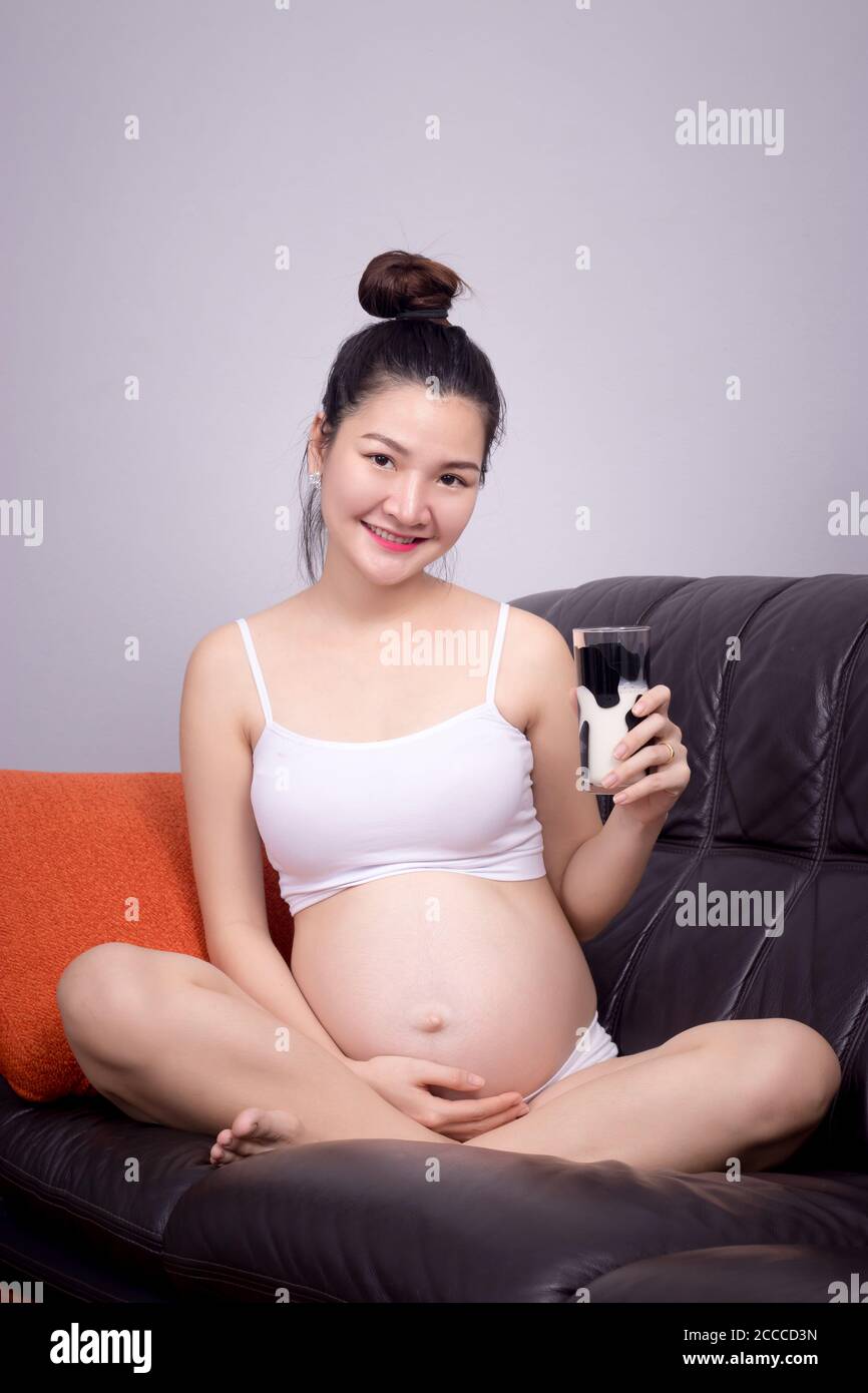 Concetto sano incinta. Un ritratto di una bella donna incinta asiatica beve latte dal bicchiere in mano. Bella Asia modello femminile nei suoi 20 Foto Stock