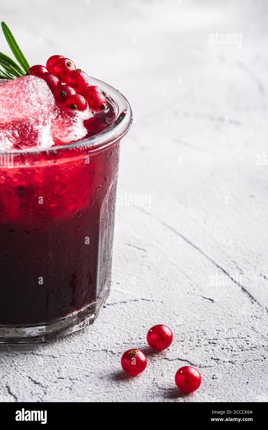 Cocktail di frutta fresca ghiacciata in vetro, rinfrescante bevanda estiva al ribes rosso con foglia di rosmarino su fondo di pietra in cemento, vista angolare Foto Stock