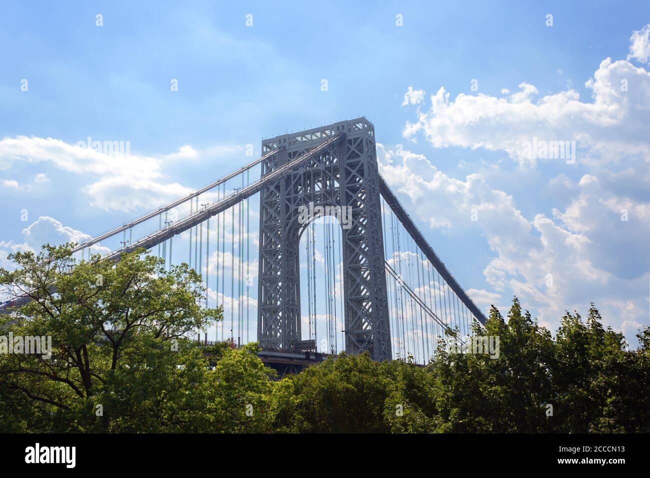 La torre di sospensione laterale di Manhattan del George Washington Bridge, un ponte sospeso a due piani, sopra le cime degli alberi contro un cielo blu e le nuvole Foto Stock