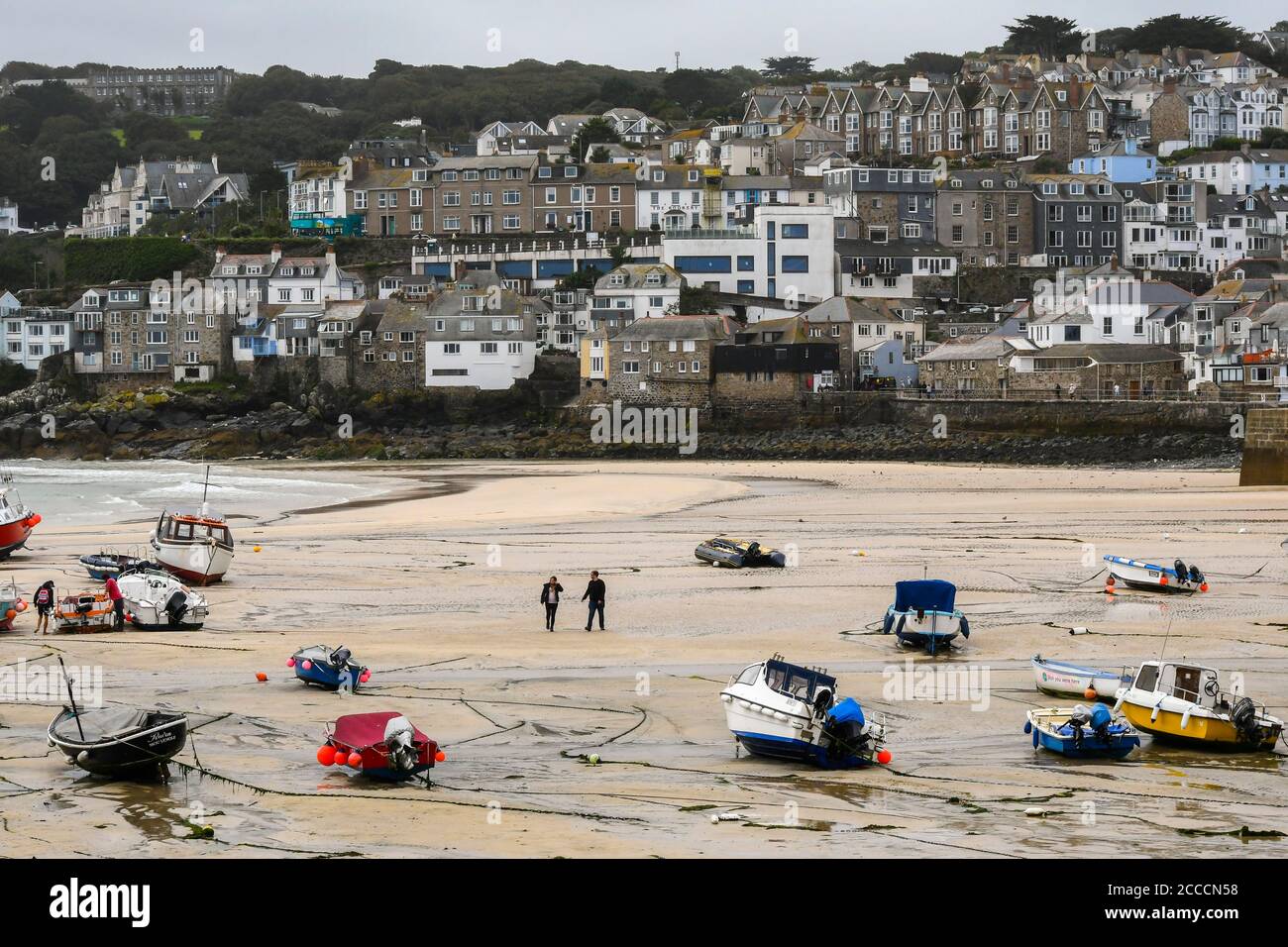 St Ives, Cornovaglia, Regno Unito. 21 agosto 2020. Regno Unito Meteo. Una coppia che cammina attraverso la sabbia tra le barche nel porto mentre la marea esce presso la località balneare di St Ives in Cornovaglia in una giornata di sole frizzante. Picture Credit: Graham Hunt/Alamy Live News Foto Stock