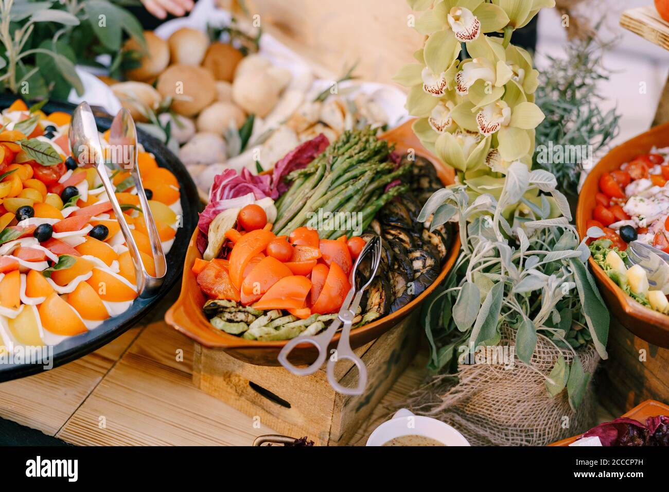 Piatti con caprese e verdure stufate sul tavolo con panini e fiori in pentole. Foto Stock