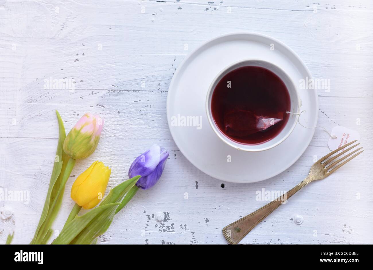 Tulipano blu fresco e tazza di tè rosso alle erbe / Donna versa il tè rosso caldo in una tazza su una tazza bianca tavolo di legno Foto Stock