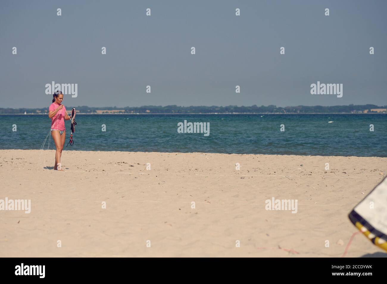 Donna di mezza età che prepara un aquilone su una spiaggia tropicale per surf in una calda giornata estiva sulla sua vacanza annuale Foto Stock