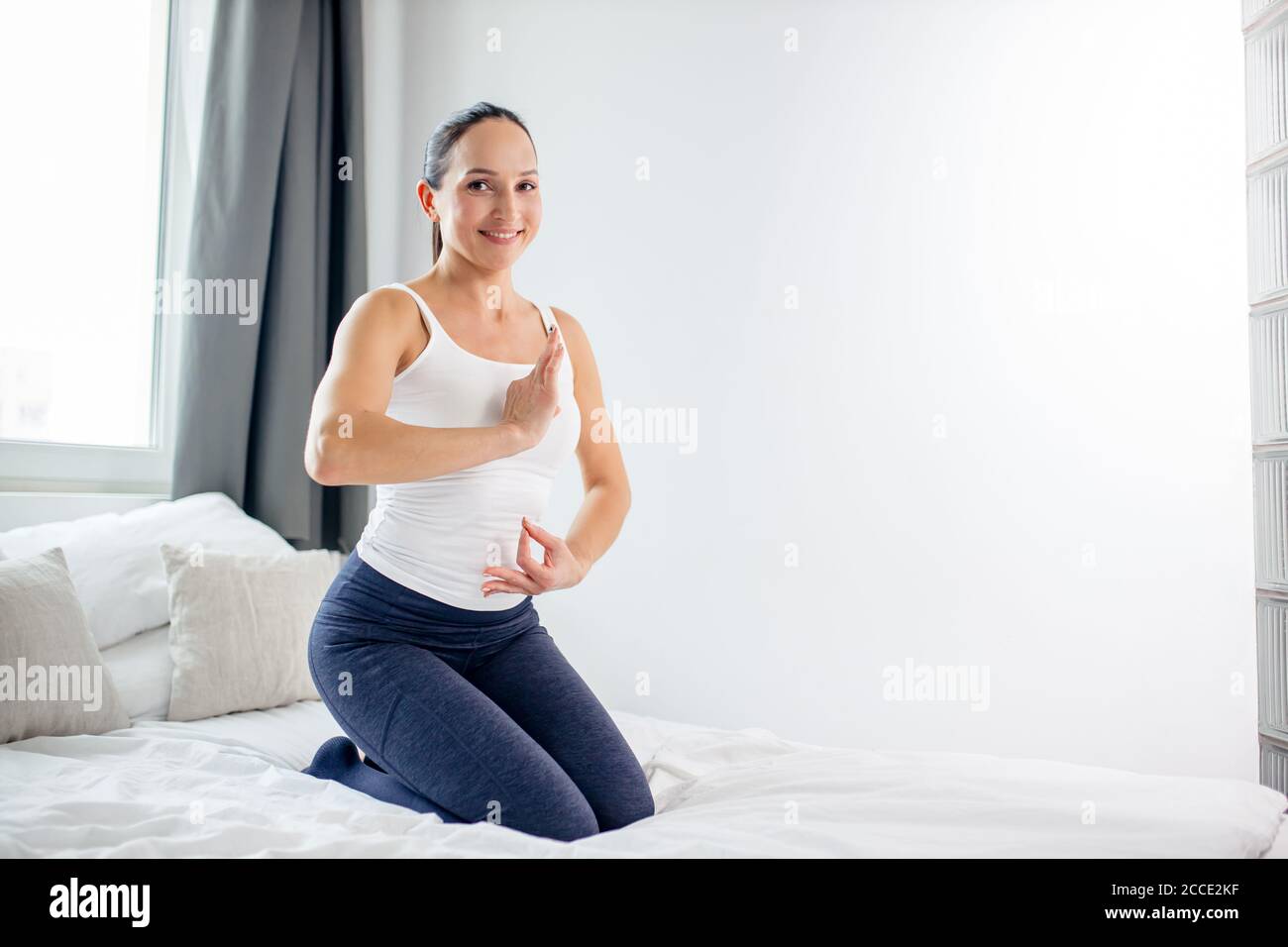 giovane donna felice sedersi in posa yoga sul letto, attraente donna godere di praticare yoga e meditare ogni mattina, mantenere la calma. stile di vita sano, wellbei Foto Stock