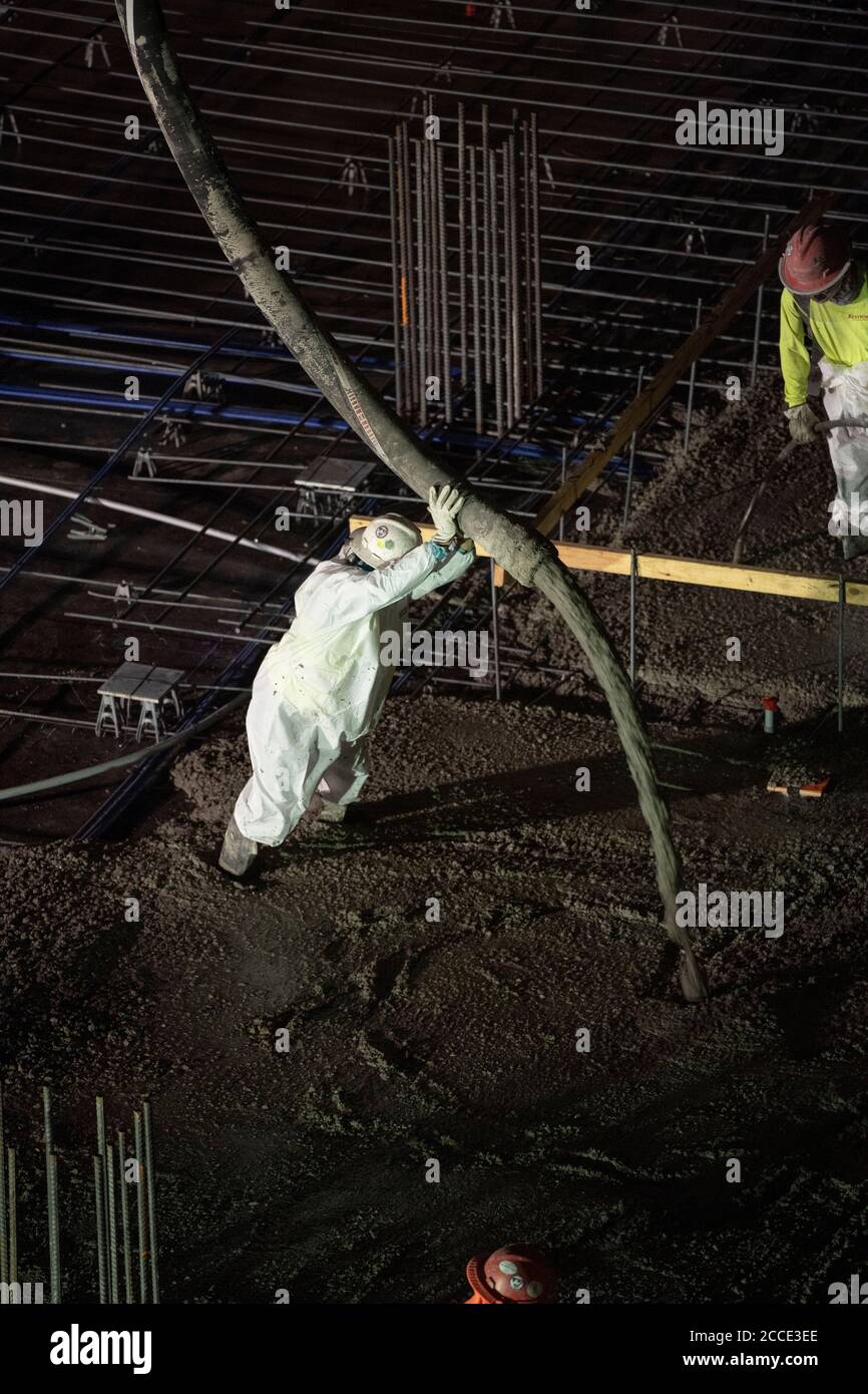 Austin, TX USA 25 luglio 2020: Il calcestruzzo pompato scorre attraverso un tubo sul pavimento di un garage di parcheggio, parte di un edificio a 53 piani in costruzione, durante una notte-time pour vicino al centro di Austin,. Foto Stock