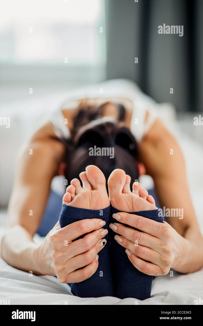 foto ravvicinata delle giovani gambe femminili mentre soing si esercita a letto a casa, stile di vita sano e concetto di yoga Foto Stock