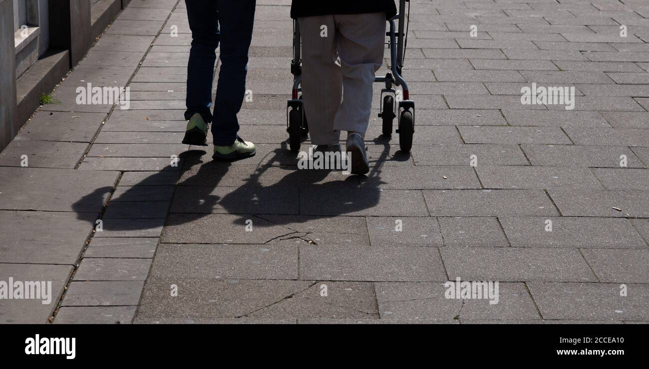 Closeup delle gambe di un maschio adulto che prende a. cammina con una donna anziana con assistenza per camminare Foto Stock
