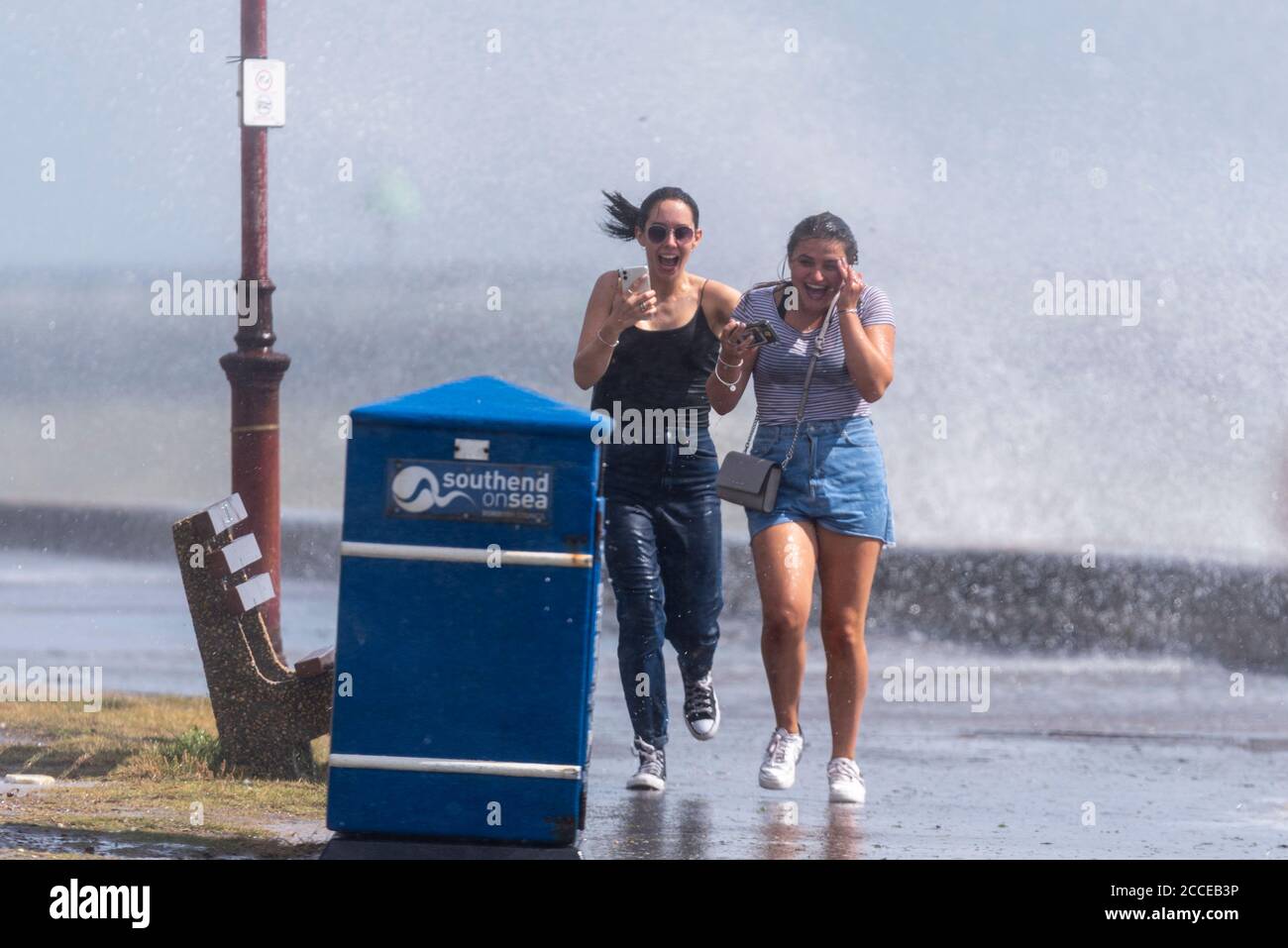 Due giovani femmine bianche che corrono attraverso onde schiaccianti a Southend on Sea, Essex, UK, durante gli alti venti di Storm Ellen, bagnandosi, bevendo Foto Stock