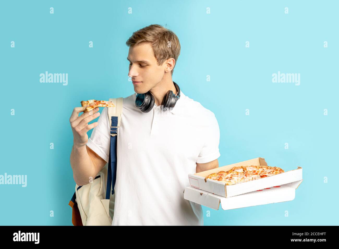 attraente uomo caucasico piacevole con pizza, andando a provare cibo gustoso fatto in azienda di consegna, trasportandolo da corrieri. sfondo blu Foto Stock