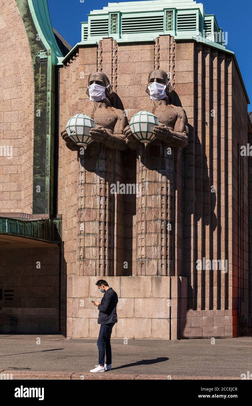 La compagnia ferroviaria finlandese ricorda di utilizzare maschere facciali a causa della seconda ondata di pandemia di coronavirus. Enormi statue di granito indossano anche maschere. Foto Stock