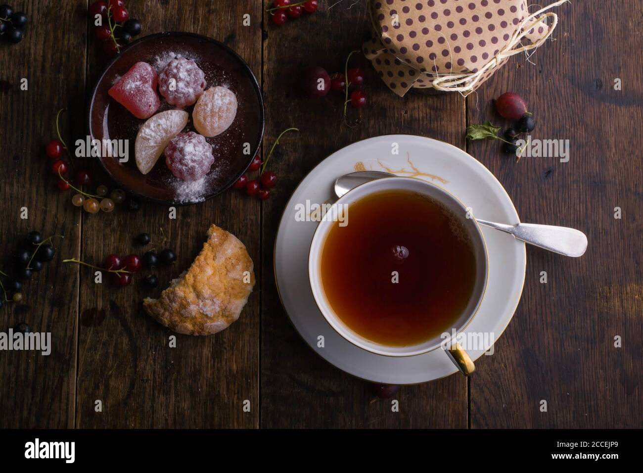 Colazione estiva. Tazza di tè d'epoca con decorazione d'oro e marmellata figurata sul vecchio tavolo di legno su cui giacciono le bacche Foto Stock