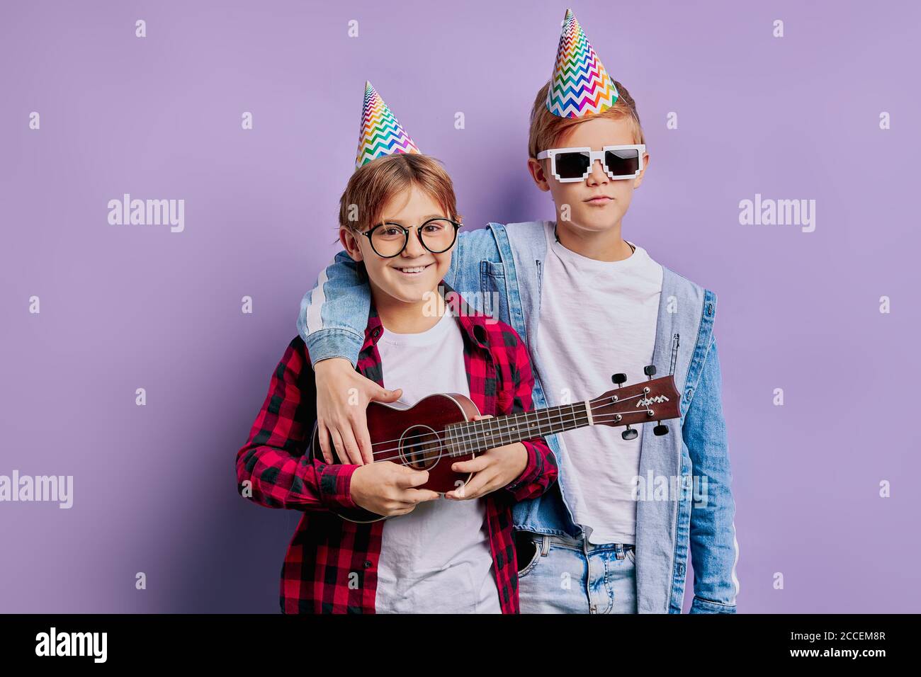ritratto di bei ragazzi di compleanno felice indossando cappello di vacanza sulla testa e tenendo ukulele, esecuzione di musica. amicizia, bambini, con compleanno Foto Stock