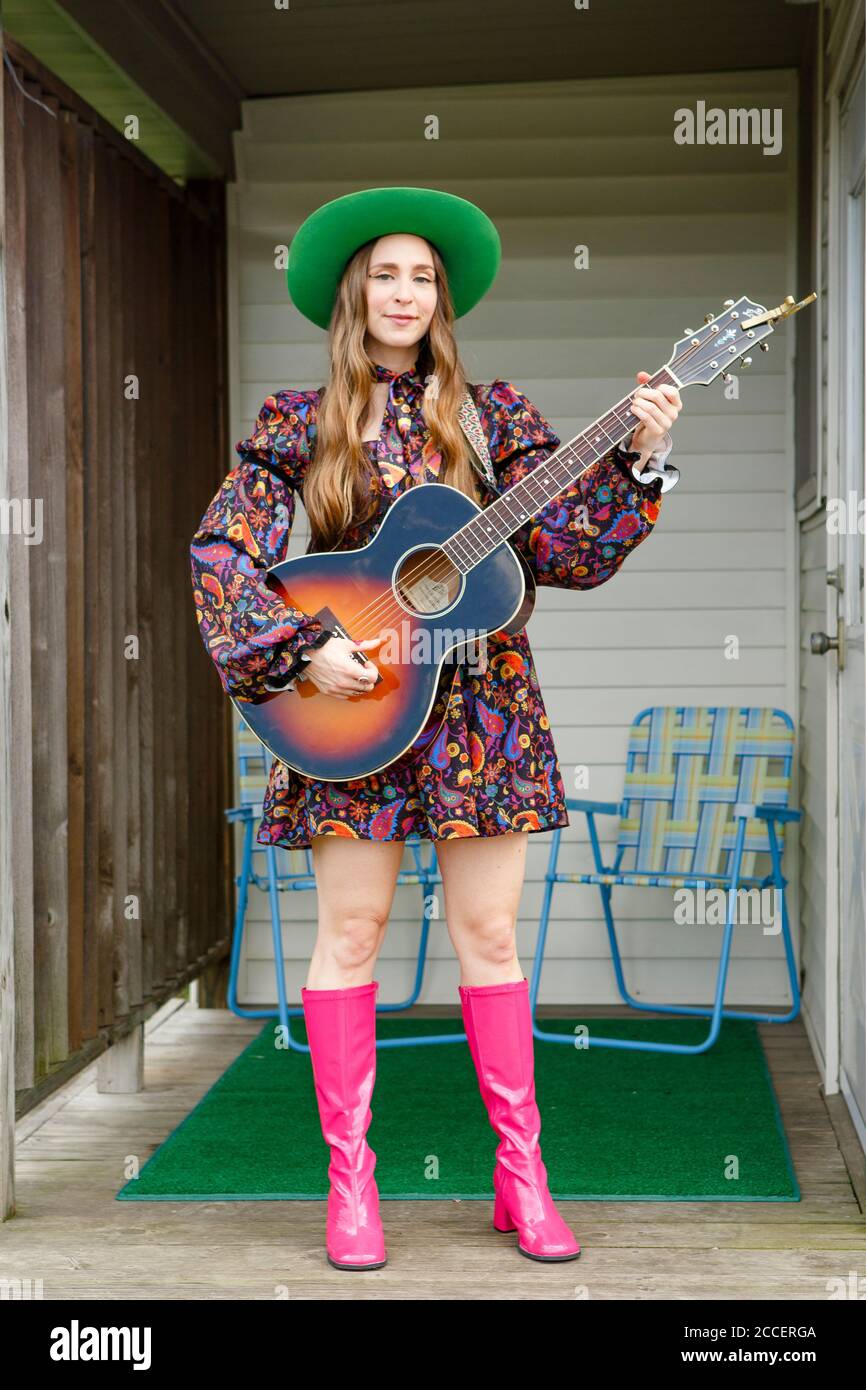 Una donna elegante con capelli lunghi e supporti per chitarra acustica sul portico Foto Stock