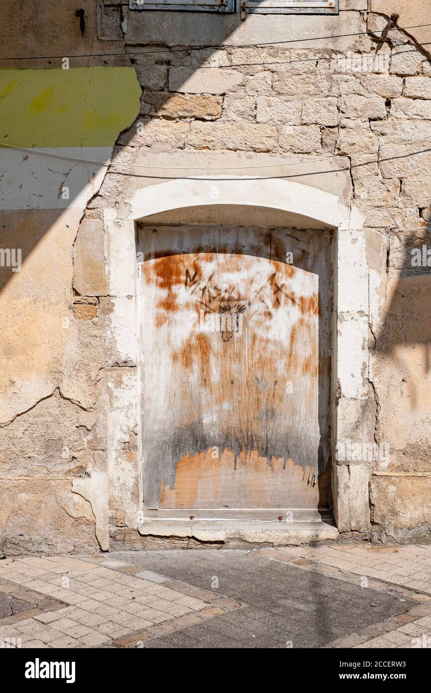 Porta in legno intemperie con graffiti su una facciata in pietra naturale con intonaco sgretolante Foto Stock