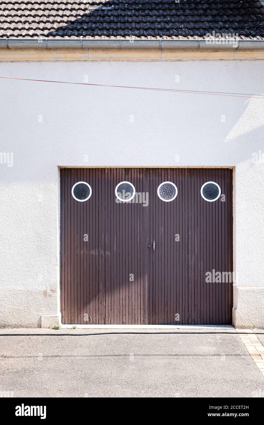 porta garage di legno marrone con quattro finestre rotonde in un edificio residenziale con facciata in gesso bianco Foto Stock