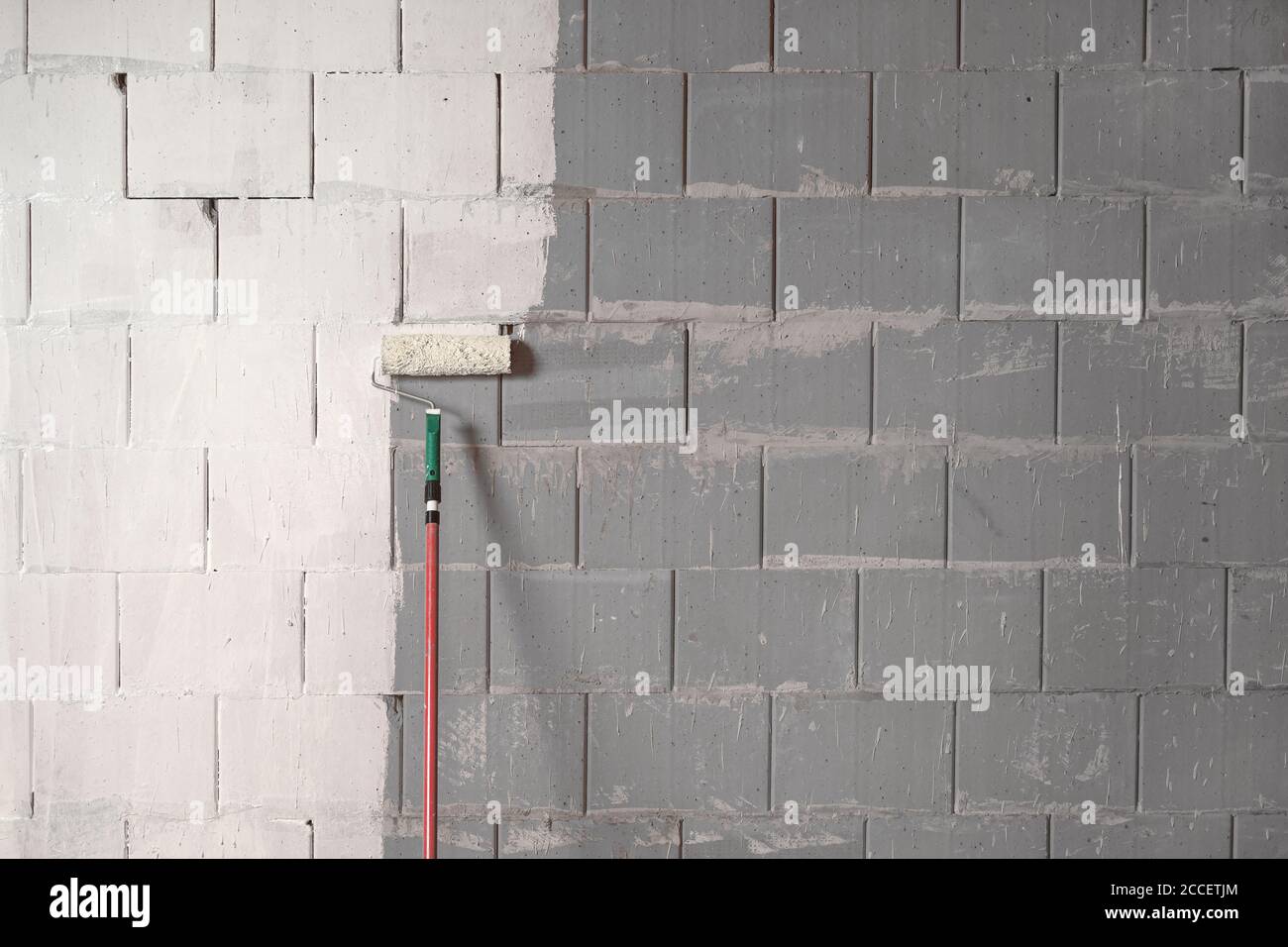 Roller sta dipingendo una parete ruvida di pietre grigie con vernice bianca, concetto di fondo per la costrizione, costruzione e ristrutturazione, spazio di copia Foto Stock