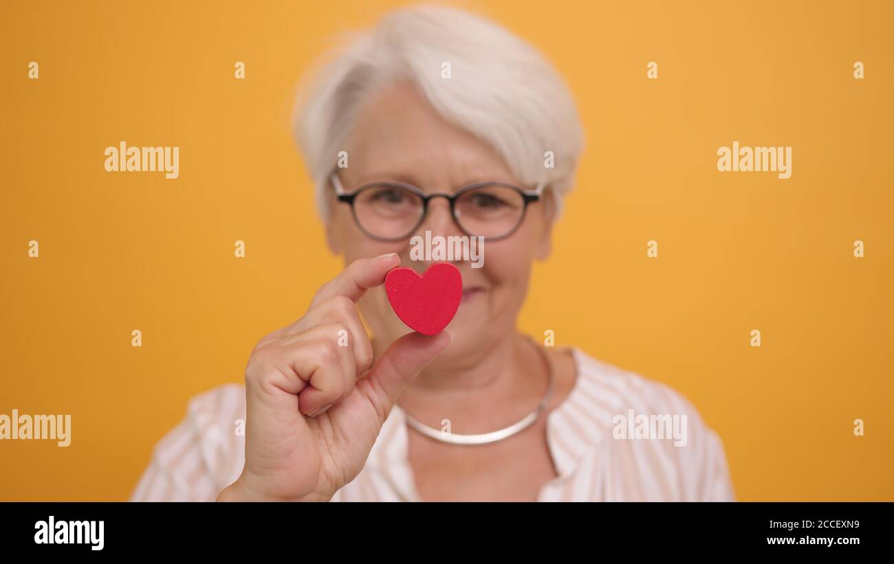 Donna anziana felice che mostra la forma del cuore tra le dita. Amore emozione e concetto di sostegno. Foto di alta qualità Foto Stock
