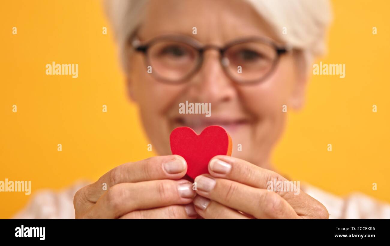 Primo piano. Donna anziana felice che mostra la forma del cuore tra le dita. Amore emozione e concetto di sostegno. Foto di alta qualità Foto Stock