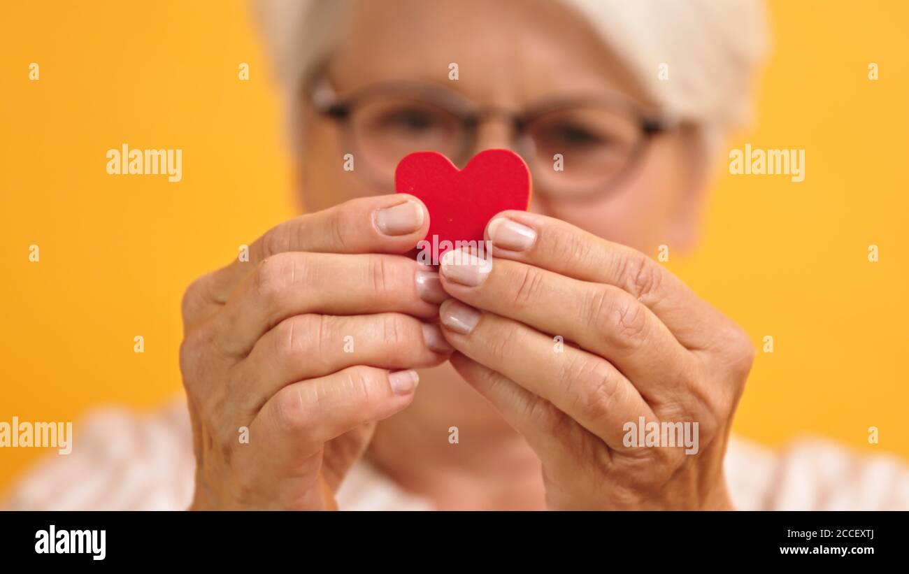 Primo piano. Donna anziana felice che mostra la forma del cuore tra le dita. Amore emozione e concetto di sostegno. Foto di alta qualità Foto Stock