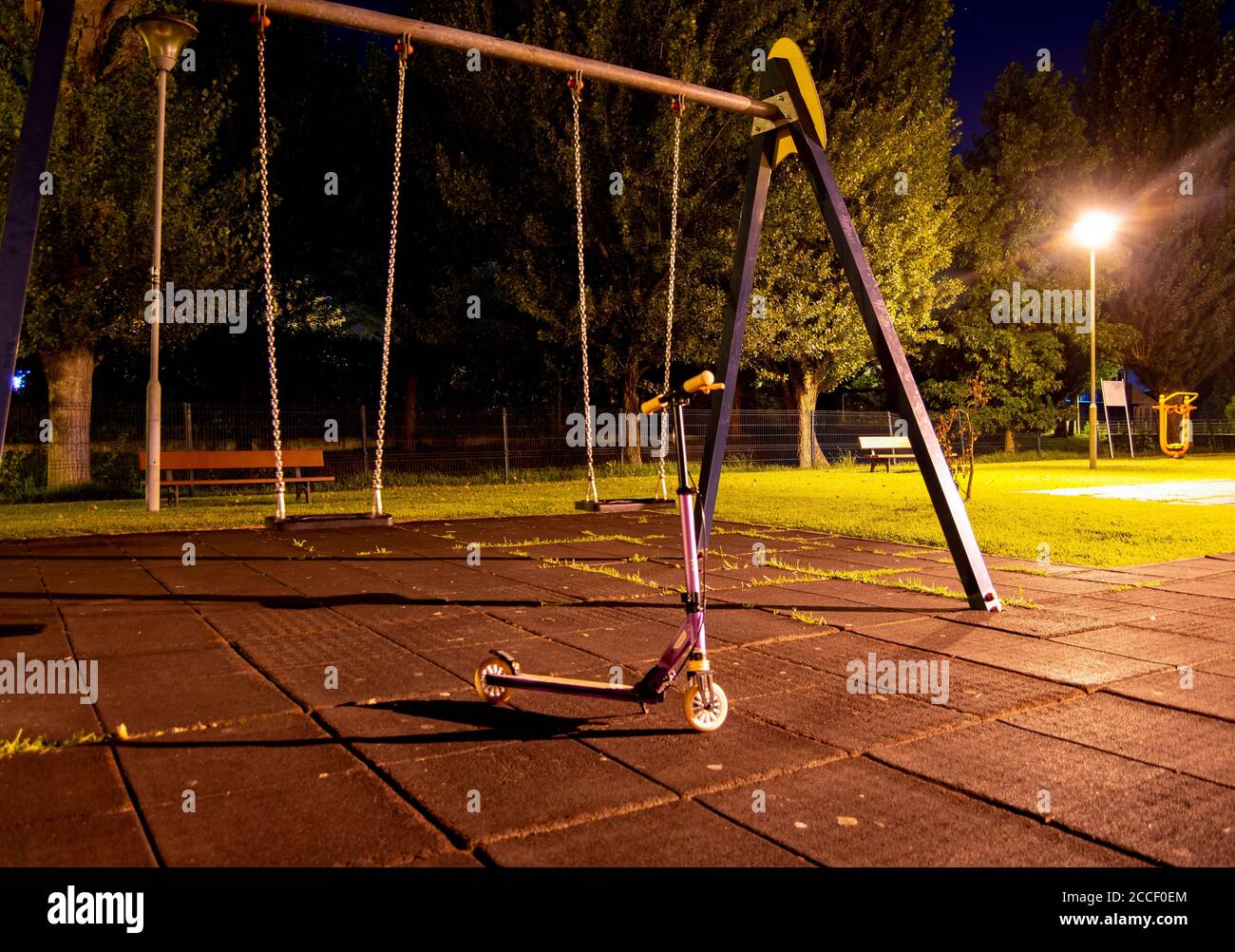 Trotinete nel parco giochi vuoto per bambini con luci accese di notte e altalene Foto Stock