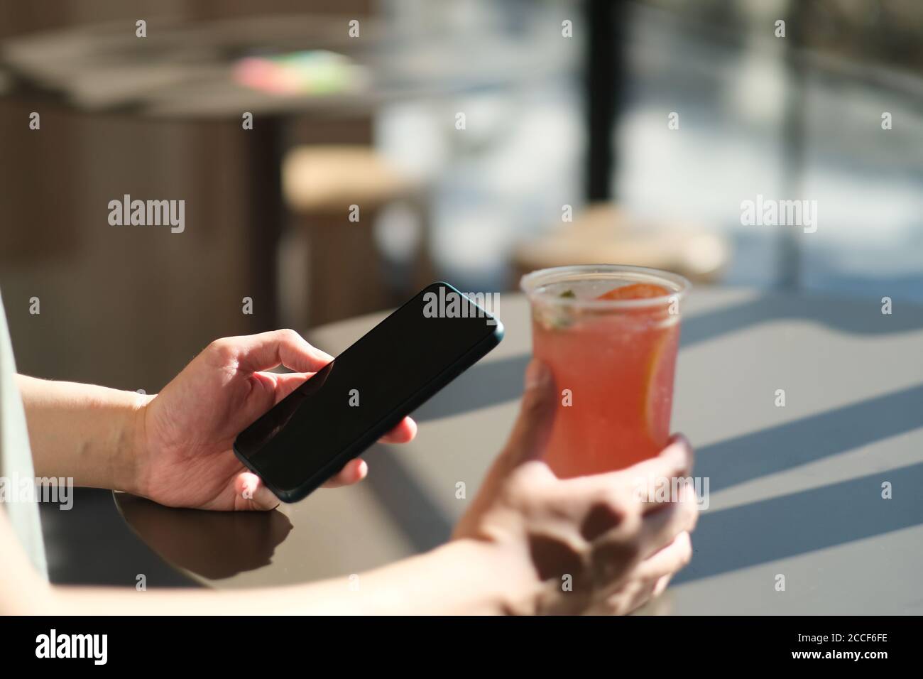 avvicinati alla mano dell'uomo utilizzando lo smartphone al bar, con una tazza di bevanda fredda sul tavolo Foto Stock