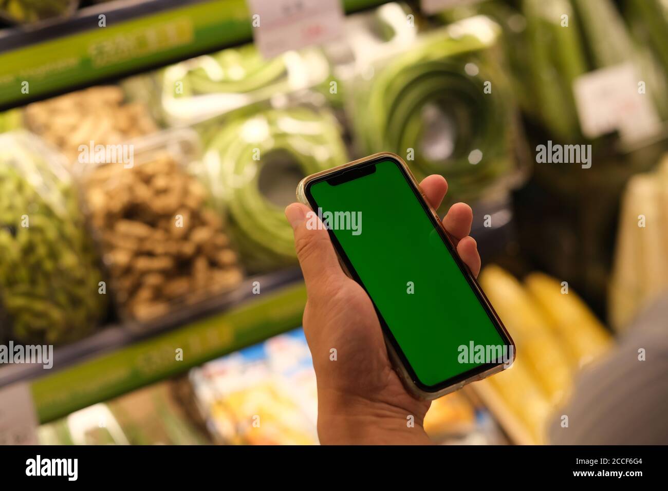 oltre la spalla di persone che tengono uno smartphone con schermo verde a. negozio di alimentari Foto Stock