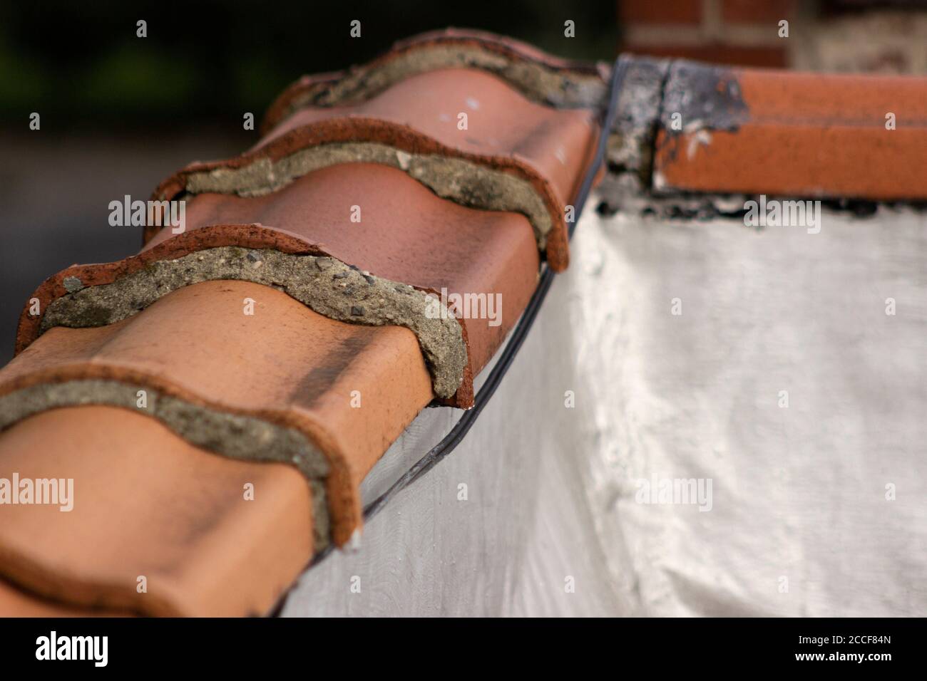 Mattonelle di terra cotta di invecchiamento con spazi riempiti di mortaio, che tappano un muro di costruzione, visto dal tetto. Foto Stock