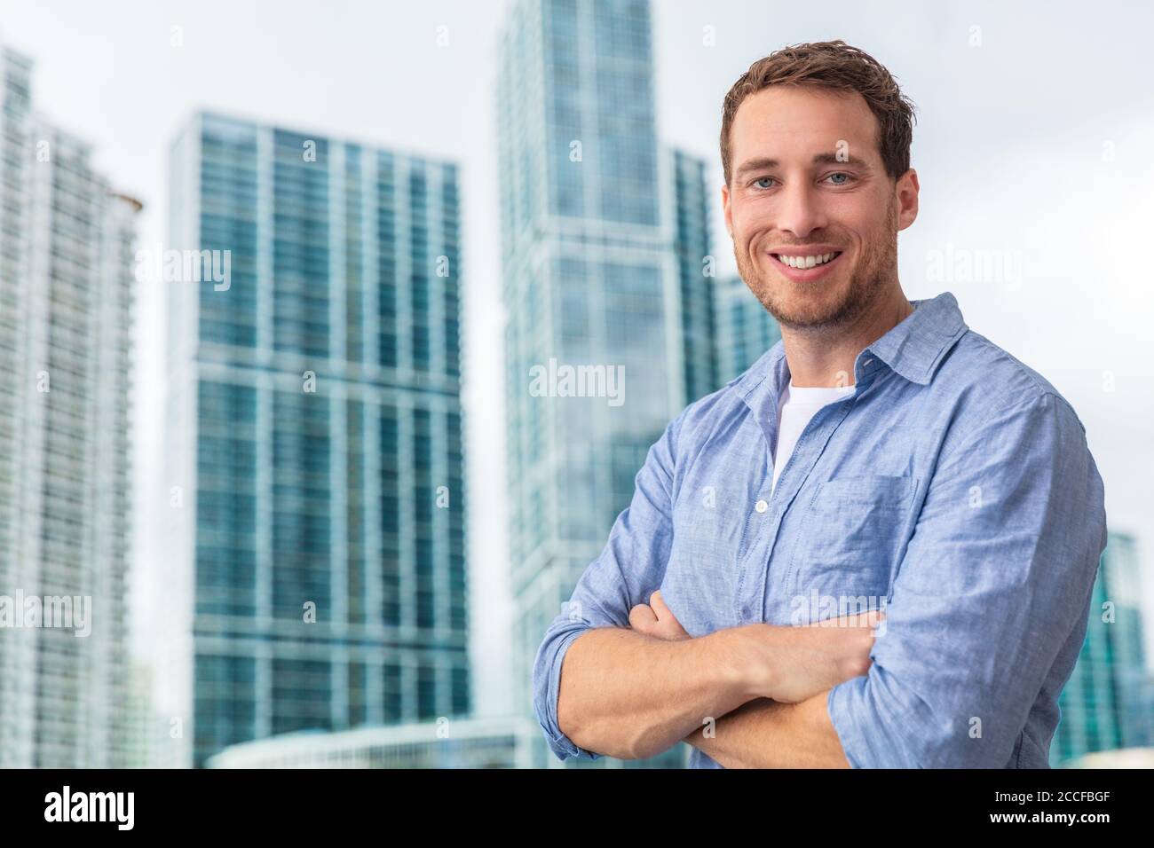 Felice giovane uomo uomo uomo uomo d'affari ritratto giovane sorridente fiducioso di fronte al moderno condominio costruzione grattacielo fuori. Gente di stile di vita della città Foto Stock