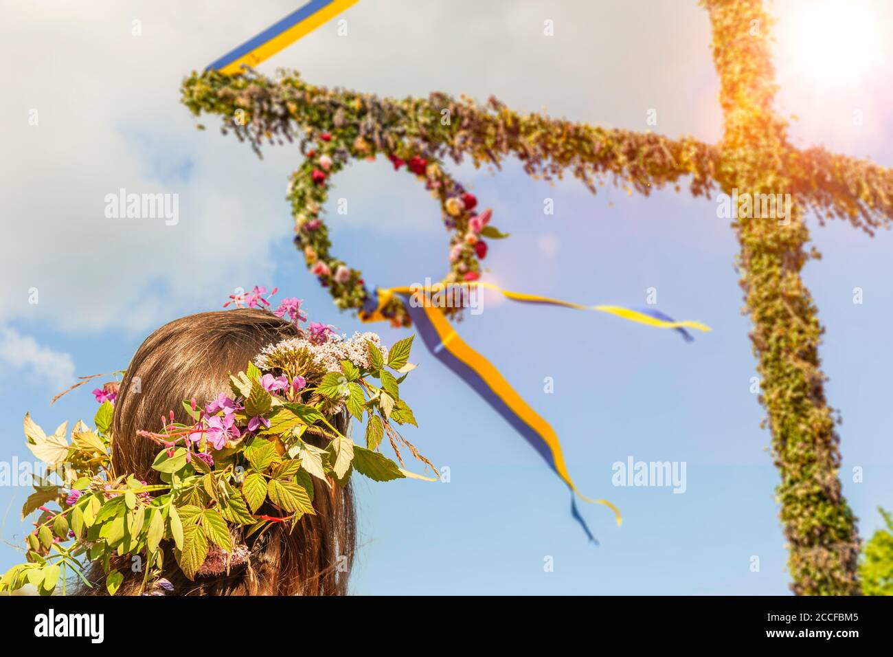 Giovane donna con corona di fiori sull'albero di metà estate in Svezia Foto Stock