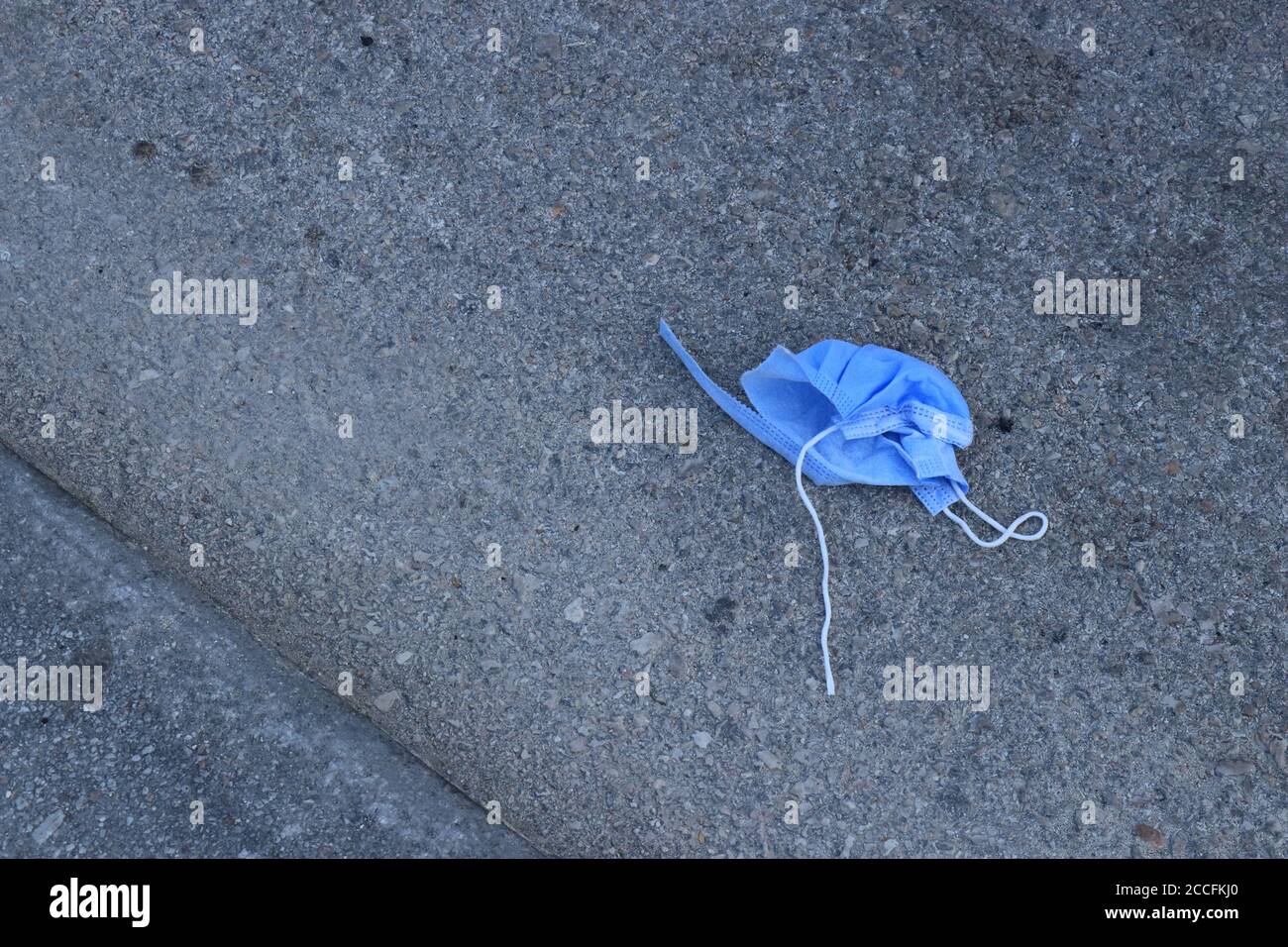 Maschera chirurgica blu utilizzata gettata sulla strada asfaltata Foto Stock