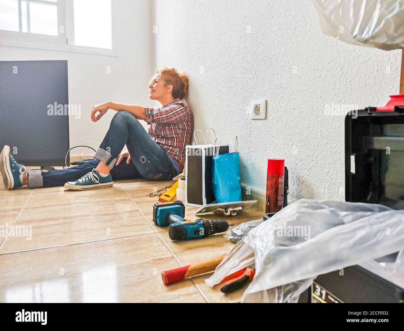 Donna felice e stanca riposano sul pavimento dopo casa lavora durante un mutuo - nuovo concetto di casa e vita - le persone godono di cambiamenti e di lavori fai da te - independde Foto Stock